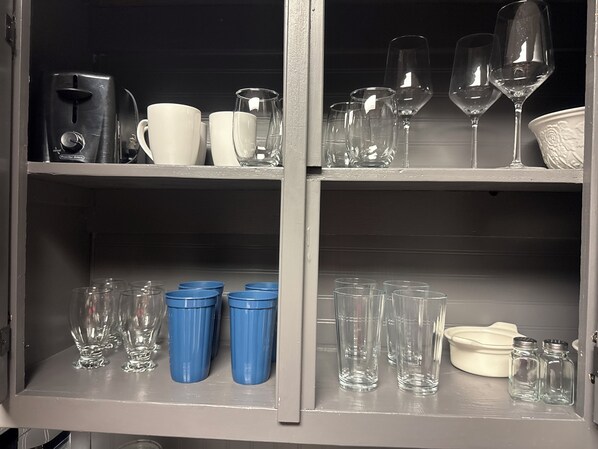 Un meuble avec des étagères contenant divers articles en verre, notamment des verres à vin, des verres à cocktail et des tasses.