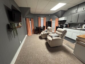 A compact living space with a seating area, kitchenette, and a flat-screen TV mounted on the wall.