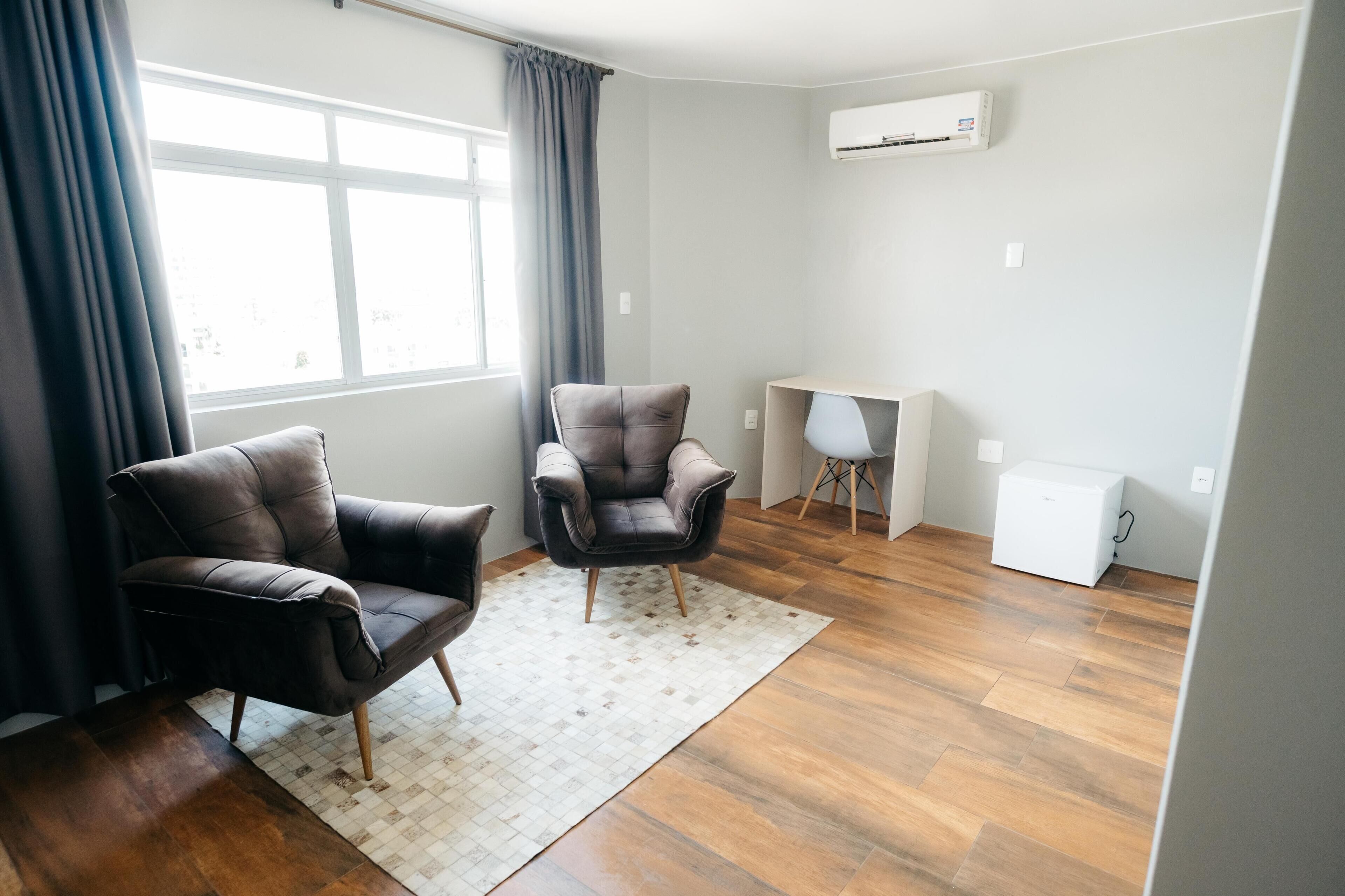 A modern living room with two leather armchairs, a small desk, and a white mini-fridge.