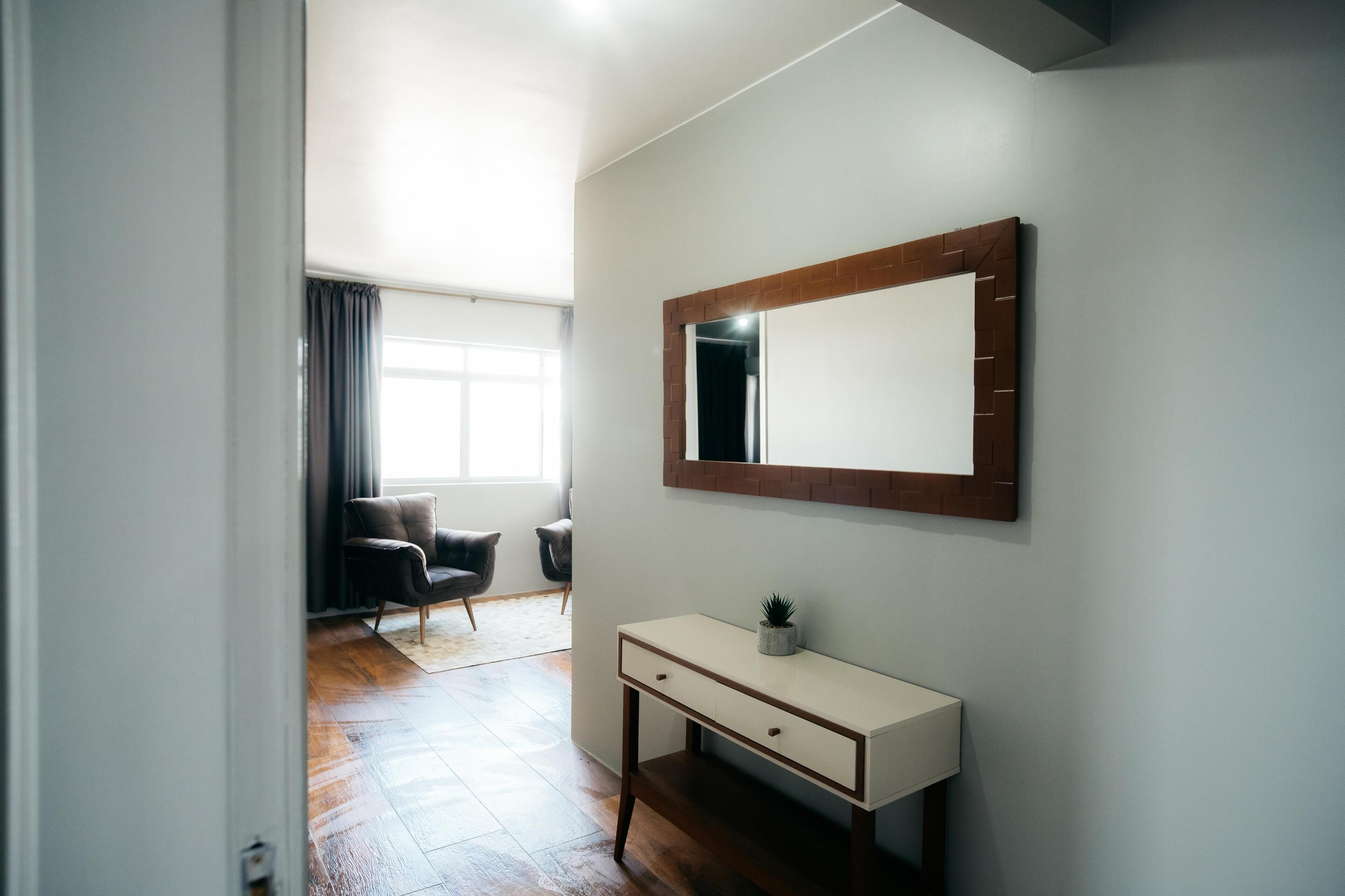 Quarto com toucador branco, espelho, planta em vaso e uma cadeira.