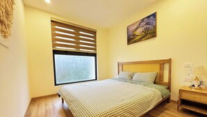 A bedroom with a large window, a bed with checkered bedding, a nightstand, and a painting on the wall. - ARIES HOUSE SAPA PROVINE, Apartment in the clouds (Sa Pa)