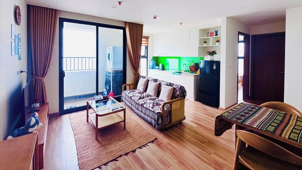 A living room with a sofa, coffee table, and a dining area with a table and chairs. There is a kitchen area with a refrigerator and a green countertop. - ARIES HOUSE SAPA PROVINE, Apartment in the clouds (Sa Pa)