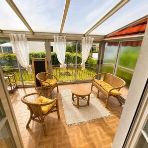 A sunroom with wicker furniture, a small table, and a view of a garden. - Maison 8p avec jardin, 2 salons & parking (Sainte-Geneviève-des-Bois)