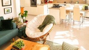 A modern kitchen with white cabinets, a dining area with chairs, and a living room with a sofa and a green chair. - Maison 8p avec jardin, 2 salons & parking (Sainte-Geneviève-des-Bois)