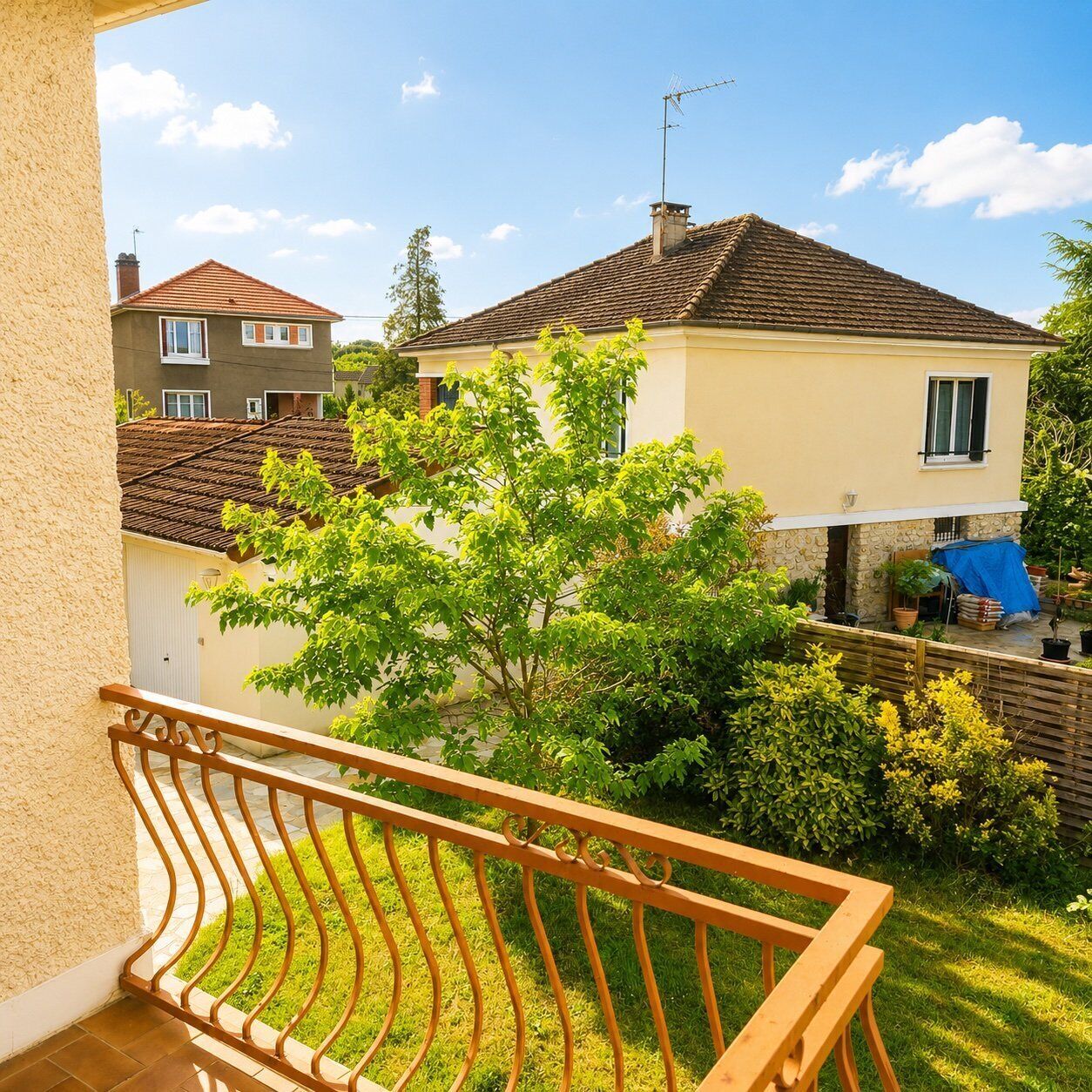 A balcony with a metal railing, a view of a house with a tiled roof, and a tree in the foreground.