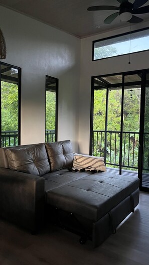 A modern living room with a sectional sofa, large windows, and a ceiling fan. - Tropical Forest Experience in Atenas (Atenas)