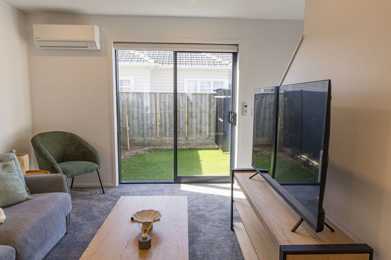 A living room with a sofa, a coffee table, a TV, and a sliding glass door leading to a backyard.