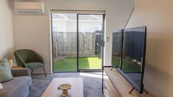 A living room with a sofa, a coffee table, a TV, and a sliding glass door leading to a backyard.