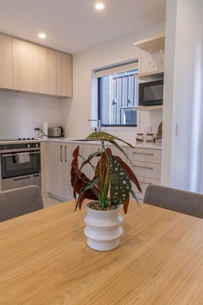Een moderne keuken met een eettafel, een potplant en een raam met zonwering.