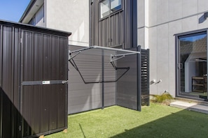 A modern building with a metal gate, a grassy yard, and a clear sky. - Stylish Townhouse for Families & Groups (Lower Hutt)