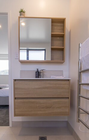 Een badkamer met een houten wastafelmeubel, een spiegel, een handdoekrek en een kleine plant op het meubel.
