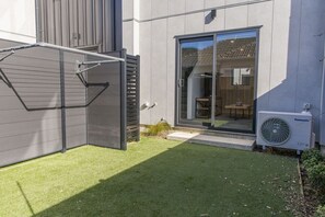 A modern building with a sliding glass door entrance, a visible outdoor seating area, and an air conditioning unit. - Stylish Townhouse for Families & Groups (Lower Hutt)