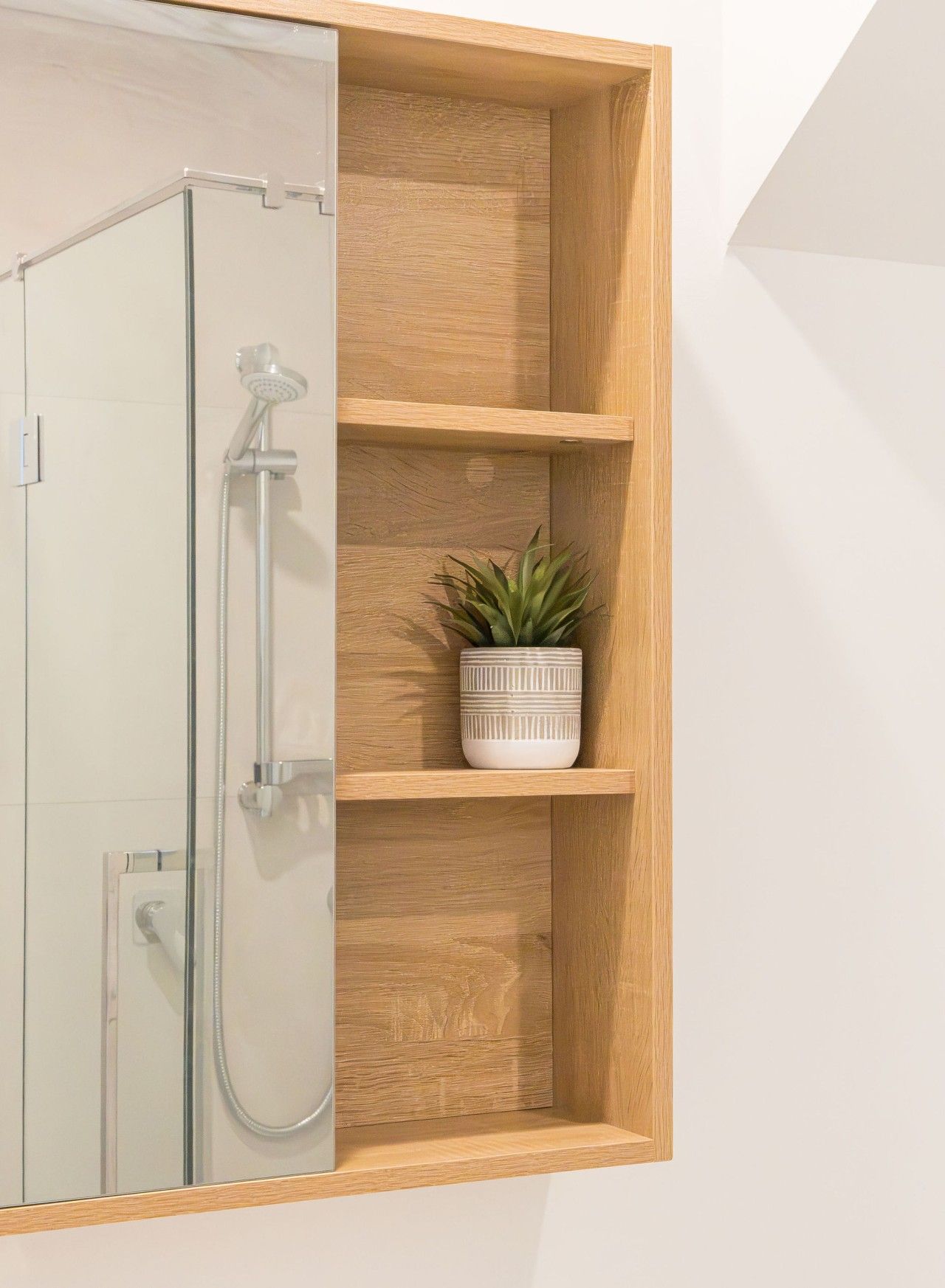 Een badkamer met een glazen douchecabine, houten planken en een potplant.