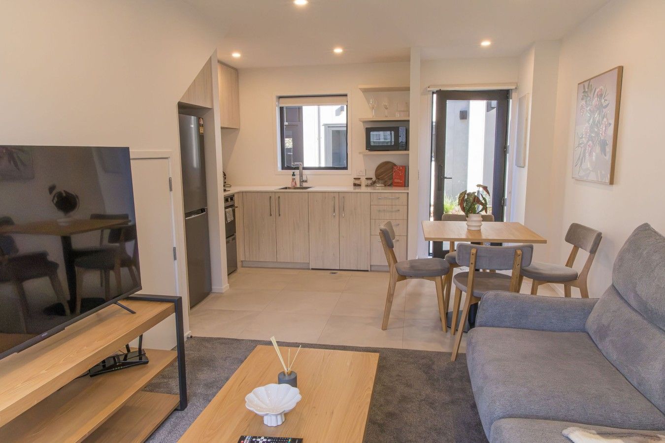 A modern living room with a flat-screen TV, a sofa, a coffee table, and a dining area with a table and chairs.