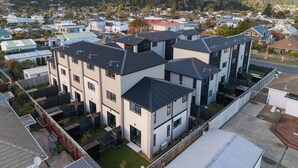 A modern residential building with multiple units, a flat roof, and a view of a residential area with houses and hills in the background. - Stylish Townhouse for Families & Groups (Lower Hutt)