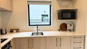 A kitchen with a window, a microwave, a toaster, and wooden cabinets. - Wellington Retreat with Private Courtyard (Lower Hutt)
