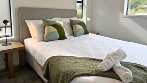 A neatly made bed with pillows, a bedside lamp, and a towel on the bed. - Wellington Retreat with Private Courtyard (Lower Hutt)