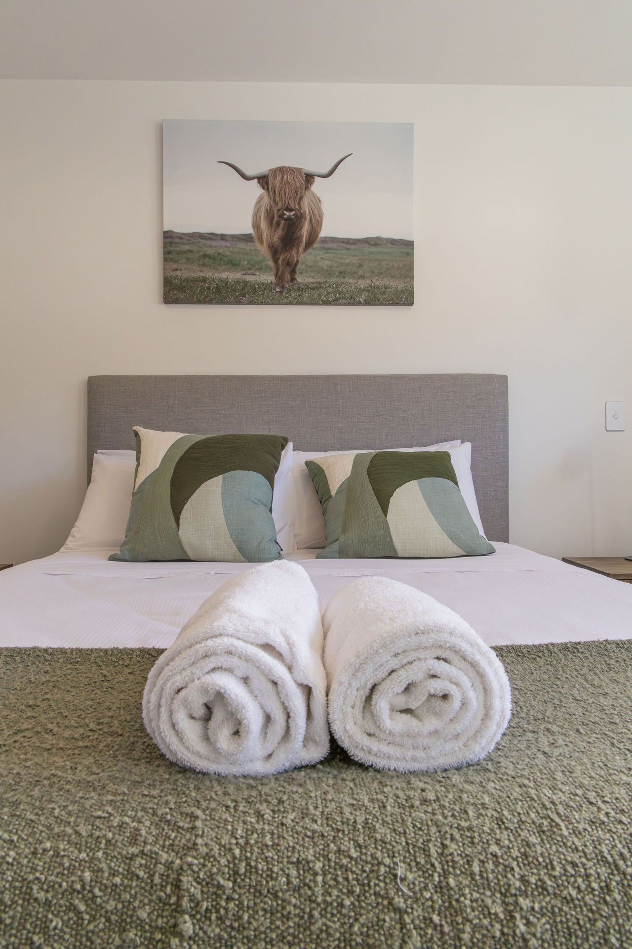 Une chambre d’hôtel avec un lit, des oreillers, une serviette roulée et un tableau représentant un taureau accroché au mur.