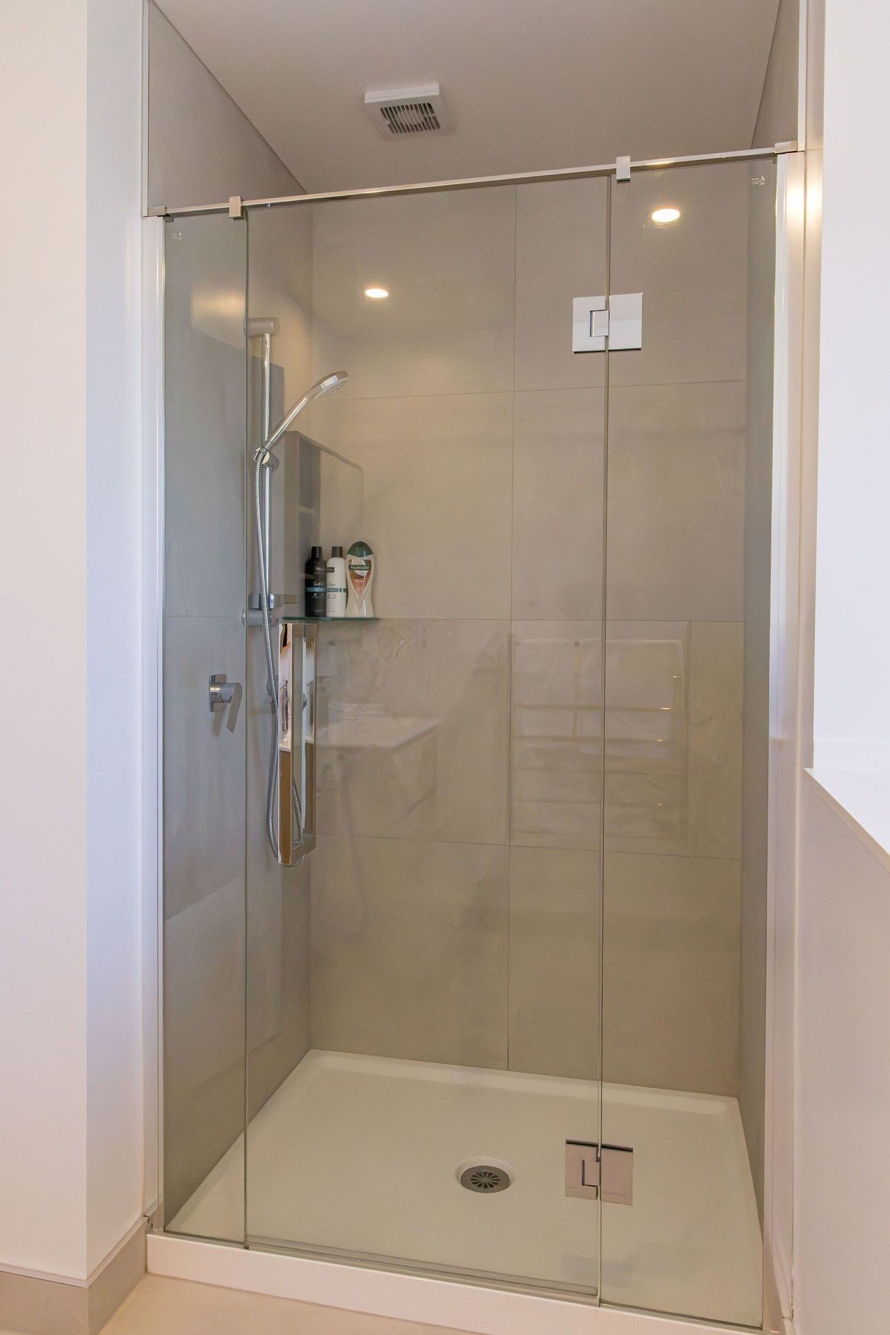 A glass-enclosed shower stall with a handheld showerhead and a handheld shower attachment.