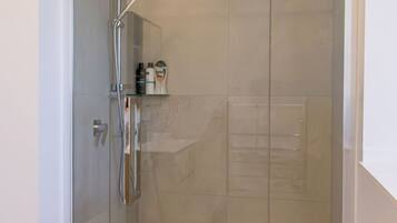 A glass-enclosed shower stall with a handheld showerhead and a handheld shower attachment.