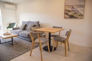 Een moderne woonkamer met een grijze bank, een houten eettafel met vier stoelen en een schilderij aan de muur.