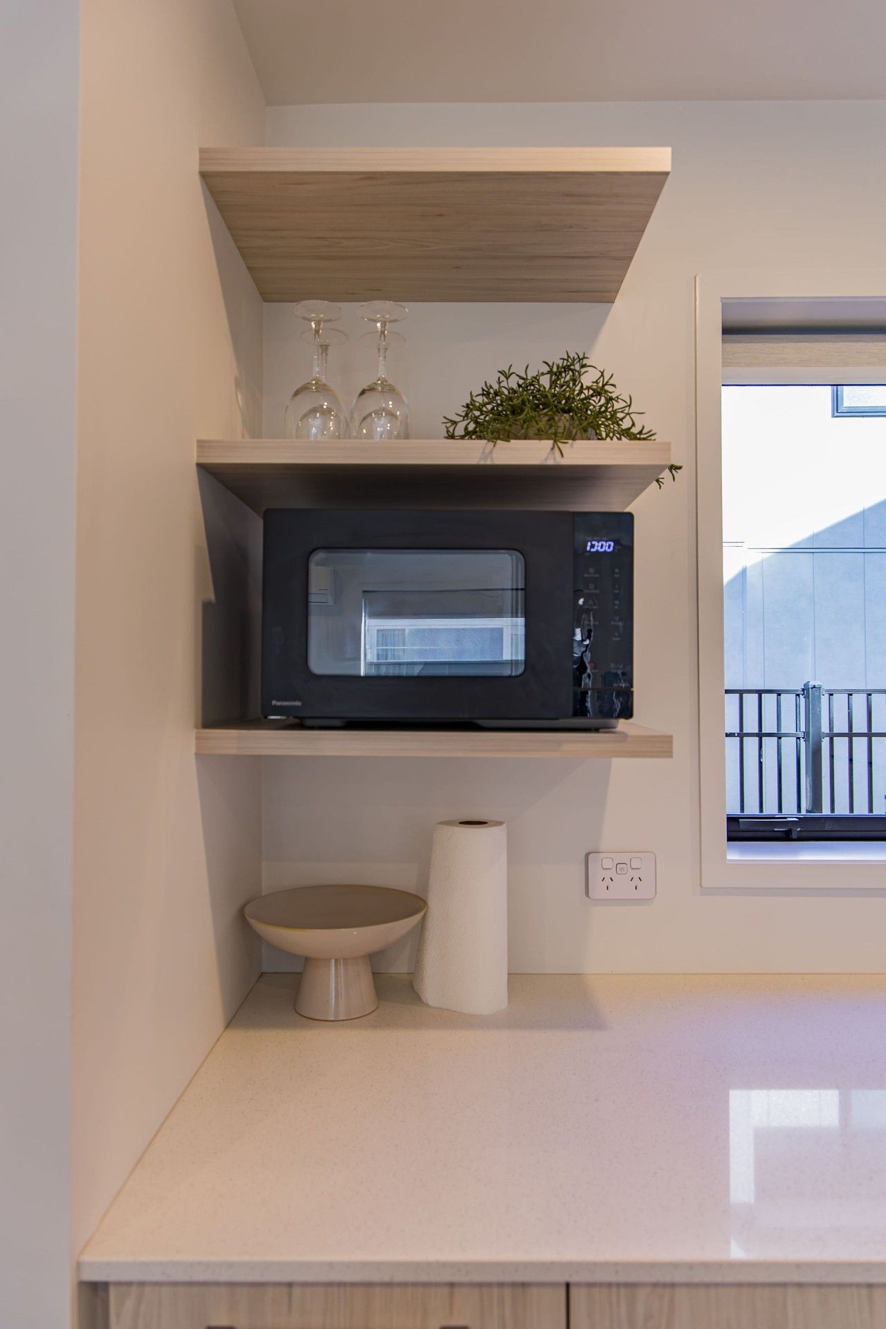 A modern kitchen with a built-in microwave, a small sink, and a window with a view of a balcony.