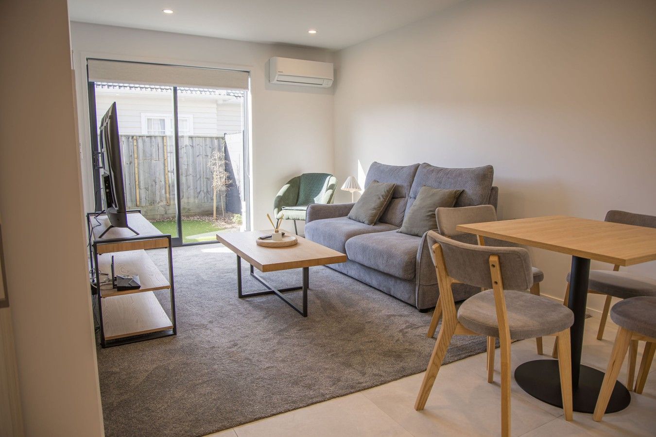 Un salon moderne comprenant un canapé, une table basse et une table à manger avec des chaises. Une porte-fenêtre coulissante donne accès à un espace patio.