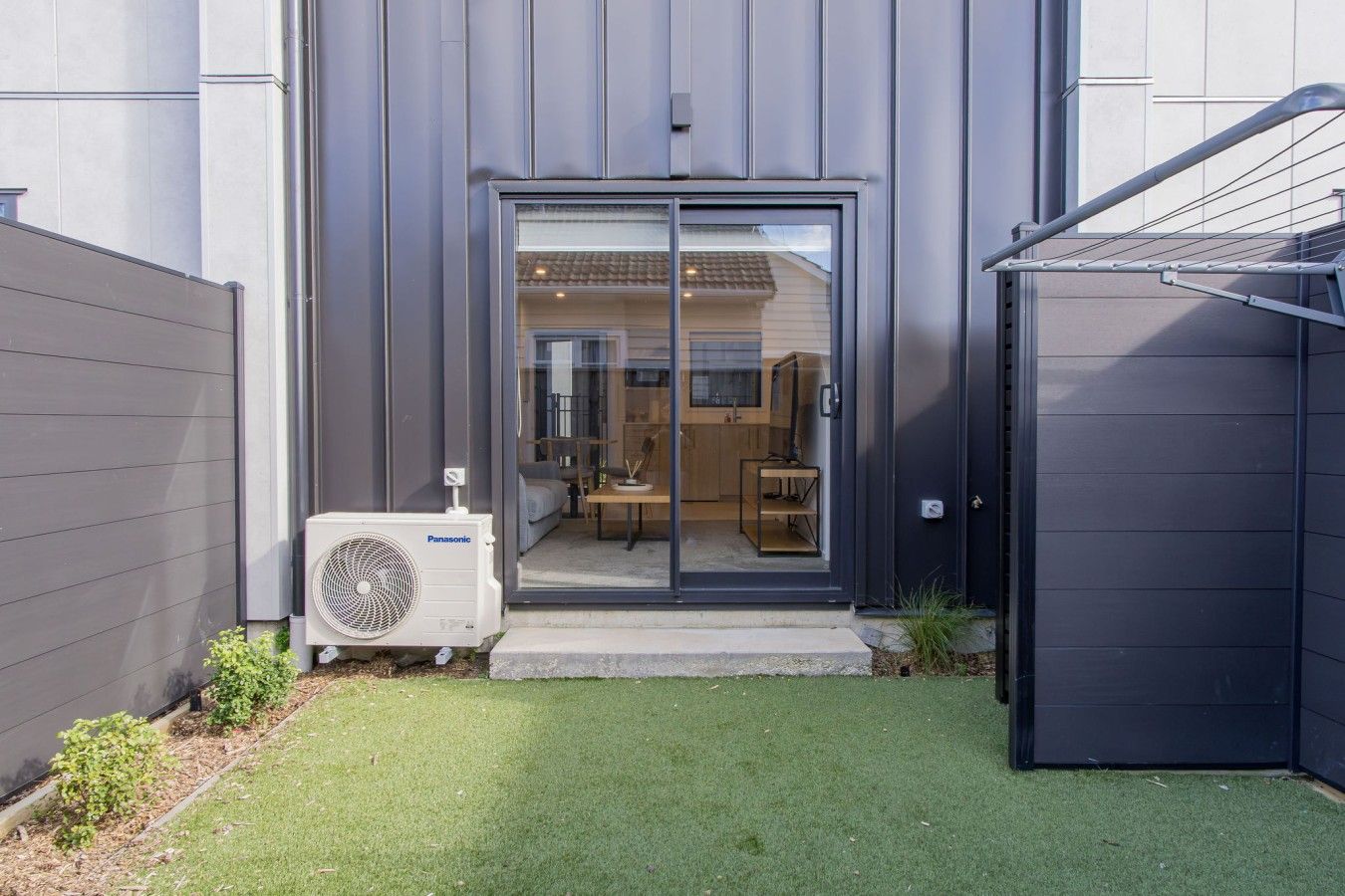 A modern building with a sliding glass door entrance, a visible kitchen area, and an air conditioning unit.