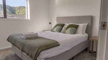 A neatly made bed with a green throw blanket, pillows, and a rolled towel.