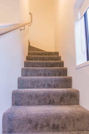 A staircase with carpeted steps and a metal handrail. - Fairfield Townhouse with Private Courtyard (Lower Hutt)