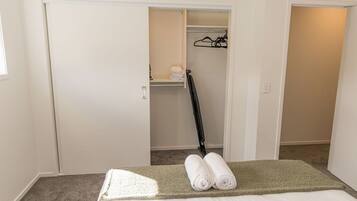 A bedroom with a bed, a green area rug, a closet with a hanging rack, and a folded towel on the bed.