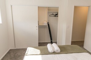 Une chambre avec un lit, un tapis vert, un placard avec une tringle et une serviette pliée posée sur le lit.