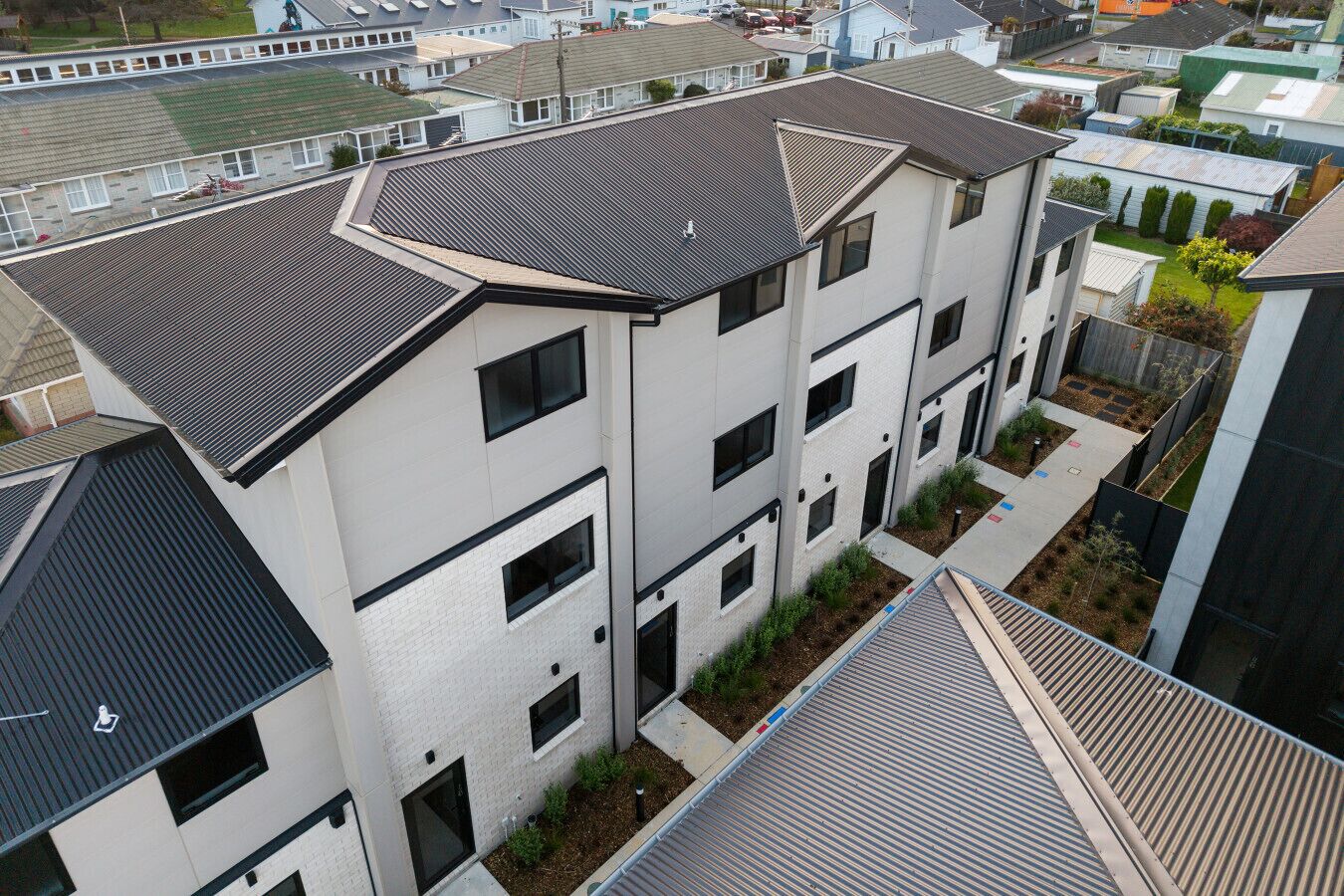 Un immeuble résidentiel à plusieurs étages, doté d’un design moderne, avec un toit plat, de grandes fenêtres et un petit espace jardin.