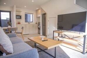 A modern living room with a sofa, a coffee table, and a television. - Modern 2BR Townhouse in Fairfield (Lower Hutt)