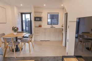A modern kitchen with a dining area, featuring a wooden table, chairs, and a potted plant. - Modern 2BR Townhouse in Fairfield (Lower Hutt)