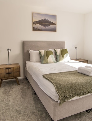 A bedroom with a bed, two bedside tables, a lamp, a blanket, and a framed picture on the wall. - Modern 2BR Townhouse in Fairfield (Lower Hutt)