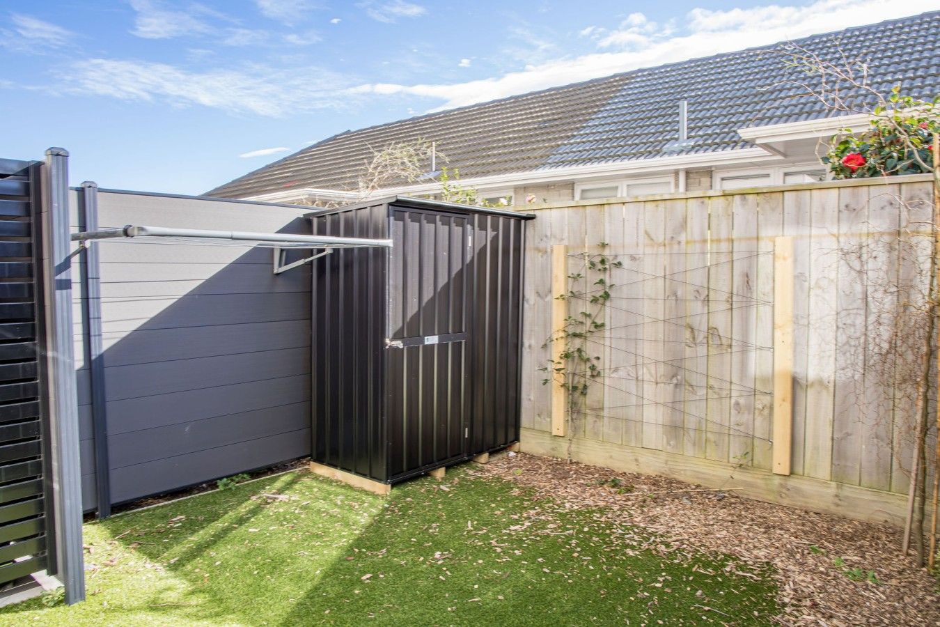 A fenced backyard with a black shed, a wooden fence, and a house in the background.