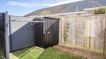 A fenced backyard with a black shed, a wooden fence, and a house in the background.