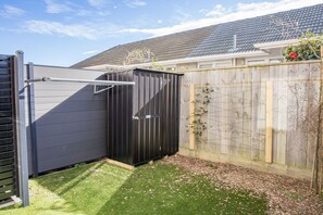 Une cour arrière clôturée avec un abri noir, une clôture en bois et une maison en arrière-plan.