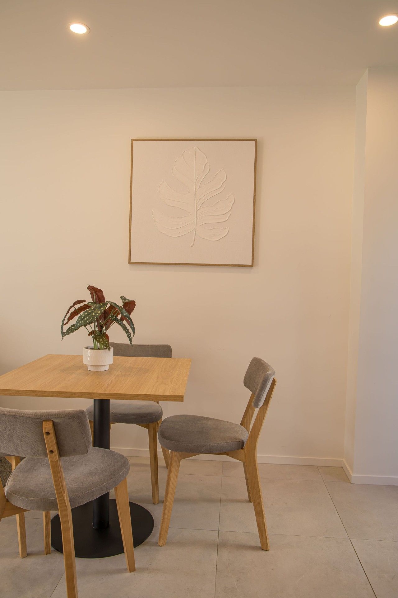 A dining area with a wooden table, four grey upholstered chairs, and a potted plant on the table.