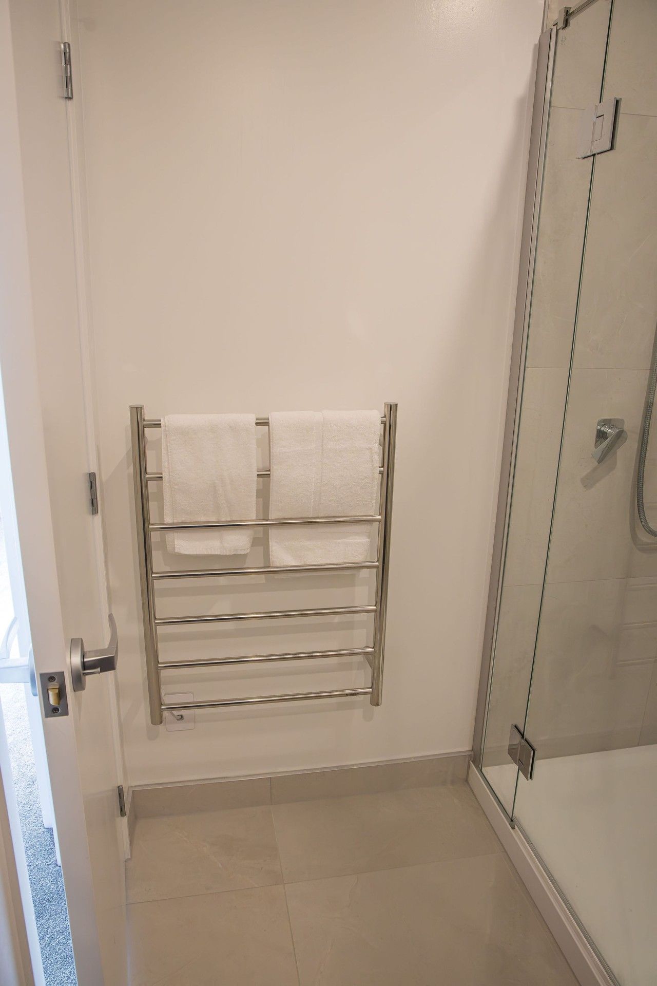 A bathroom with a glass shower enclosure, a towel rack with two towels, and a door with a handle.