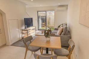 Un salon moderne comprenant un coin repas, un canapé gris, un téléviseur et une porte-fenêtre coulissante donnant sur l’extérieur.