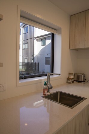 A kitchen with a window, a stainless steel sink, a toaster, and a bottle of hand soap. - Modern 2BR Townhouse in Fairfield (Lower Hutt)