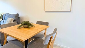 Un comedor con una mesa de madera, sillas tapizadas en gris, una planta pequeña en maceta y un cuadro abstracto grande en la pared.