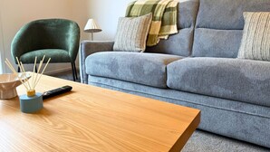 Una sala de estar con un sofá gris, una mesa de centro de madera, un sillón verde y una lámpara.