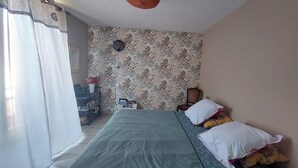 A bedroom with a bed, a chair, a small table, and a wall-mounted fan. - ROOM for 2 adults 1 h30 from TOULOUSE - Pets under -3 kg accepted. (SAINT-PROJET)