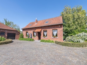 A brick house with a tiled roof, a paved driveway, and a well-maintained garden with flowering bushes.