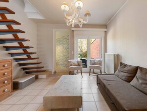 A modern living room with a staircase, a sofa, a table, and a chandelier. - Comfortable house in the heart of the village (Le Bizet)