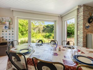 A dining area with a table set for four, large windows, and a brick wall. - Comfortable house in the heart of the village (Le Bizet)