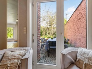 A room with a sliding glass door leading to an outdoor patio area with a brick wall, a table, and chairs. - Comfortable house in the heart of the village (Le Bizet)